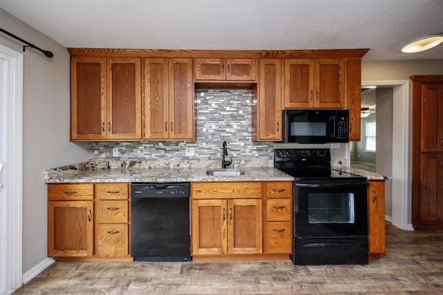 1012 28th St, Des Moines, IA 50311 - kitchen featuring black appliances, backsplash, brown cabinetry, light stone counters, and light wood-style flooring
