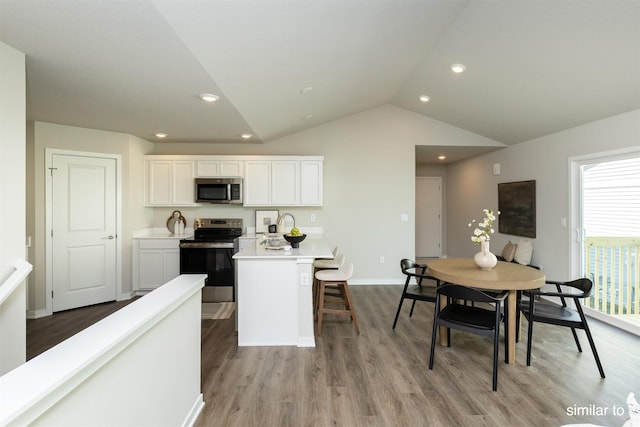 725 Linden St, Carlisle, IA 50047 - kitchen with stainless steel appliances, white cabinetry, vaulted ceiling, light countertops, and light wood finished floors