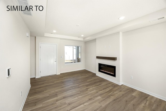2212 Legacy Dr, Norwalk, IA 50211 - unfurnished living room featuring wood finished floors, recessed lighting, a glass covered fireplace, and a tray ceiling