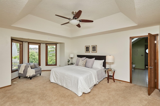 2216 NW 136th St, Clive, IA 50325 - bedroom featuring a tray ceiling, light colored carpet, a textured ceiling, connected bathroom, and ceiling fan