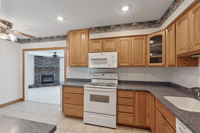 2441 Hull Ave, Des Moines, IA 50317 - kitchen featuring white appliances, ceiling fan, dark countertops, glass insert cabinets, and a fireplace