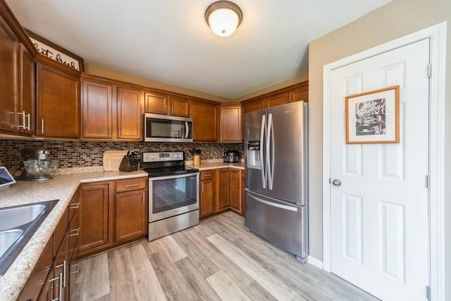 150 SE Hazelwood Dr, Waukee, IA 50263 - kitchen with stainless steel appliances, brown cabinetry, light wood-style floors, decorative backsplash, and light countertops