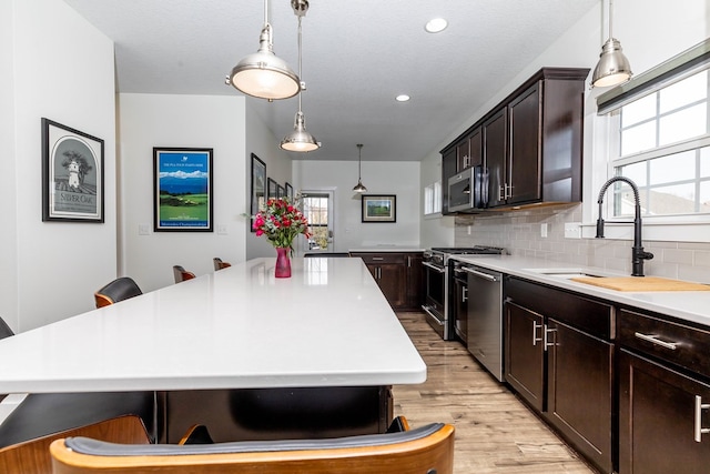 5477 S Prairie View Dr, West Des Moines, IA 50266 - kitchen featuring appliances with stainless steel finishes, light wood-style flooring, light countertops, dark brown cabinets, and recessed lighting