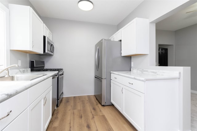2537 Maple St, Des Moines, IA 50317 - kitchen featuring stainless steel appliances, white cabinets, light wood-style floors, a peninsula, and light stone counters