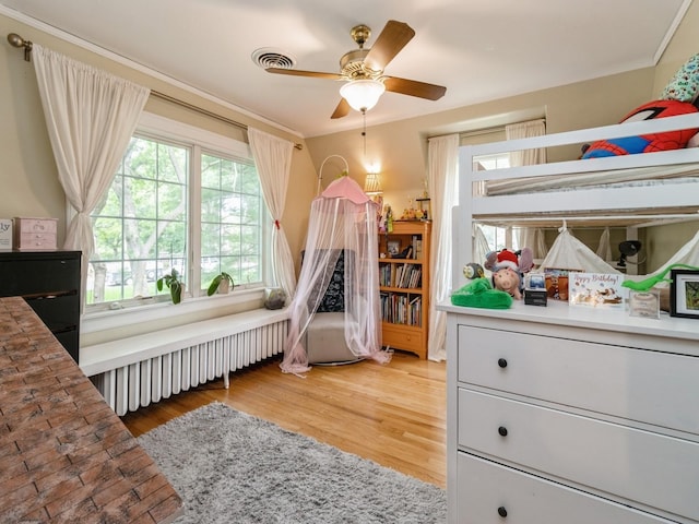 215 Foster Dr, Des Moines, IA 50312 - bedroom featuring radiator heating unit, multiple windows, light wood-style flooring, and a ceiling fan