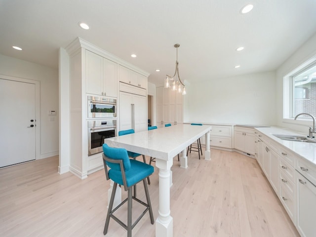 1863 Glen Oaks Dr, West Des Moines, IA 50266 - kitchen featuring double oven, a kitchen bar, light wood-style floors, white cabinets, and recessed lighting