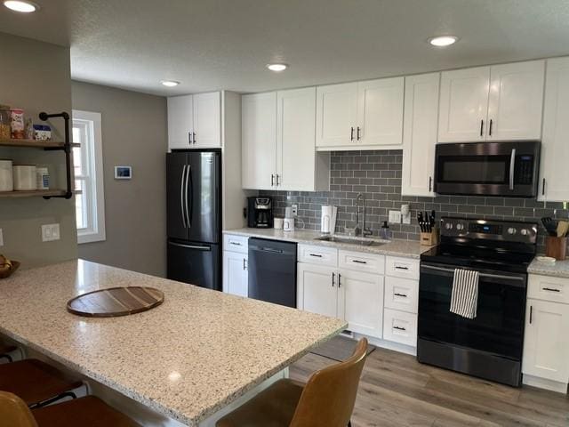 316 NW Linden St, Ankeny, IA 50023 - kitchen featuring black appliances, a breakfast bar area, white cabinets, tasteful backsplash, and recessed lighting