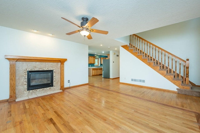 117 4th St NW, Altoona, IA 50009 - unfurnished living room featuring light wood finished floors, a ceiling fan, stairway, a tiled fireplace, and a textured ceiling