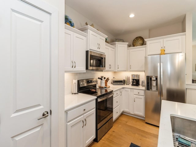 2206 SW Westwood St, Ankeny, IA 50023 - kitchen featuring appliances with stainless steel finishes, white cabinets, light countertops, light wood-type flooring, and tasteful backsplash