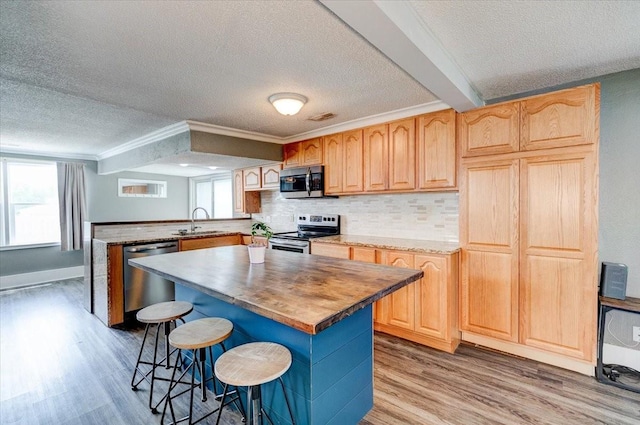 911 E 1st Ave, Indianola, IA 50125 - kitchen with stainless steel appliances, a textured ceiling, a peninsula, light wood-type flooring, and a breakfast bar area