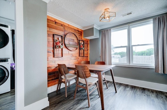 911 E 1st Ave, Indianola, IA 50125 - dining space featuring stacked washer and clothes dryer, wooden walls, a textured ceiling, wood finished floors, and crown molding