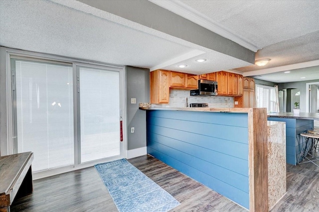 911 E 1st Ave, Indianola, IA 50125 - kitchen with stainless steel microwave, a textured ceiling, dark wood-style flooring, a peninsula, and a breakfast bar