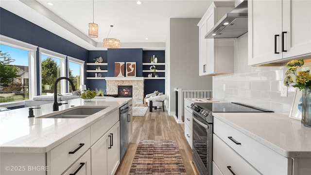 780 NE Badger Ln, Waukee, IA 50263 - kitchen featuring wall chimney exhaust hood, stainless steel appliances, light wood-style floors, a center island with sink, and a fireplace