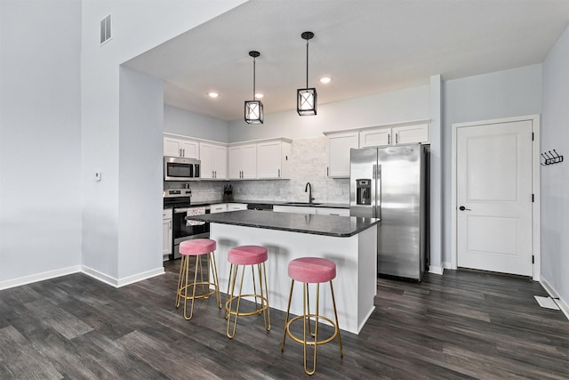 481 10th St, Waukee, IA 50263 - kitchen with stainless steel appliances, dark wood-style flooring, dark countertops, a kitchen island, and white cabinets
