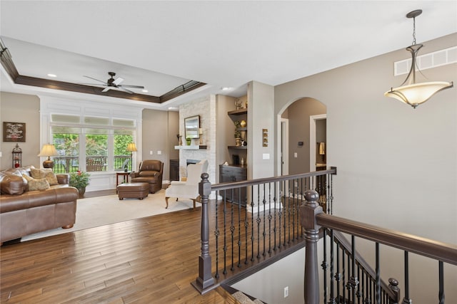 800 NE Badger Ln, Waukee, IA 50263 - living area with a ceiling fan, a raised ceiling, a stone fireplace, arched walkways, and wood finished floors
