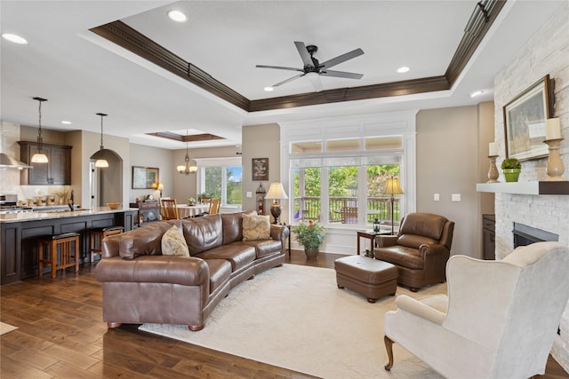 800 NE Badger Ln, Waukee, IA 50263 - living room featuring a tray ceiling, crown molding, ceiling fan, dark wood-style flooring, and a stone fireplace