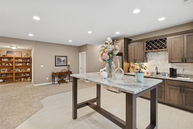800 NE Badger Ln, Waukee, IA 50263 - kitchen with recessed lighting, dark brown cabinetry, light colored carpet, light stone countertops, and a kitchen island with sink
