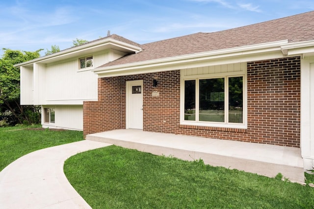 8501 NW Beaver Dr, Johnston, IA 50131 - view of exterior entry with a shingled roof, brick siding, and a yard