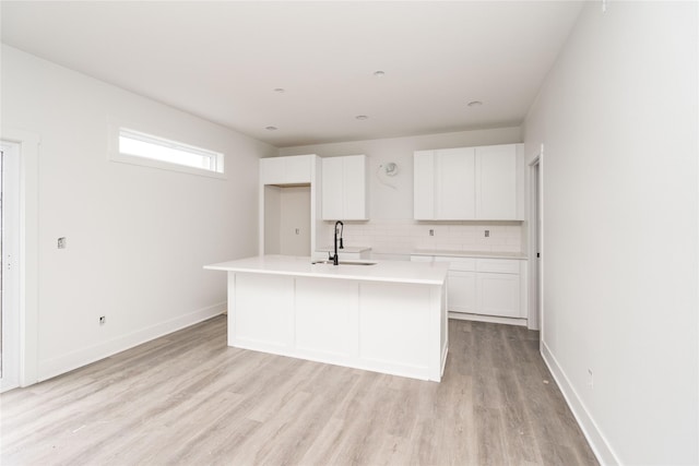 17987 Alpine Dr, Clive, IA 50325 - kitchen featuring white cabinetry, light wood-style floors, tasteful backsplash, a kitchen island with sink, and light countertops