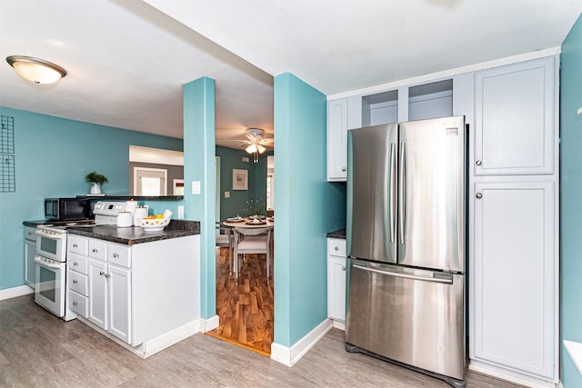 1229 9th St, Nevada, IA 50201 - kitchen with freestanding refrigerator, range with two ovens, light wood finished floors, ceiling fan, and white cabinetry