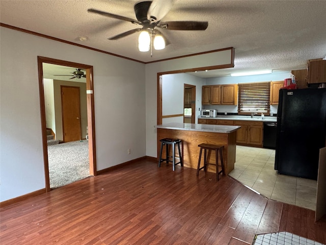 2601 Sherwood Dr, Des Moines, IA 50310 - kitchen with black appliances, a peninsula, ceiling fan, brown cabinets, and a kitchen bar