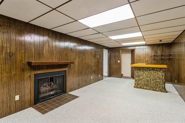 2907 Northwood Dr, Ames, IA 50010 - unfurnished living room featuring a bar, carpet floors, a fireplace with flush hearth, wood walls, and a paneled ceiling