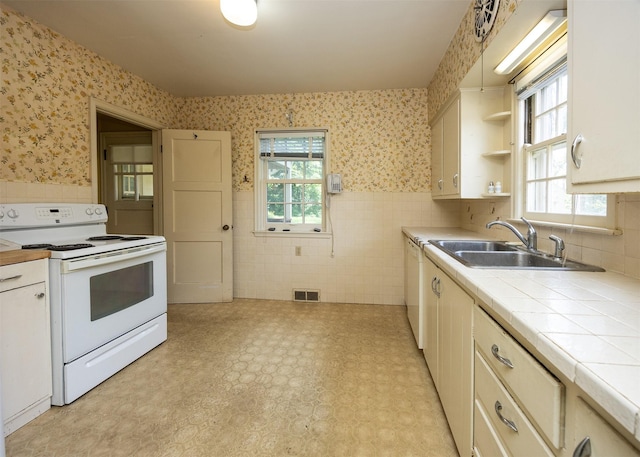5800 Pleasant Dr, Des Moines, IA 50312 - kitchen with white appliances, wallpapered walls, tile countertops, tile walls, and a wainscoted wall