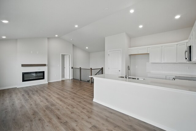 4270 Grover Woods Ln, Des Moines, IA 50317 - kitchen featuring white cabinets, stainless steel microwave, backsplash, light wood-type flooring, and vaulted ceiling