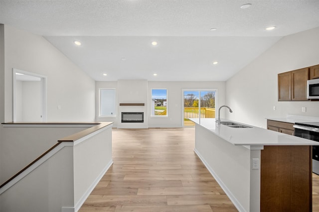 4400 Honey Bee Rdg, Des Moines, IA 50317 - kitchen with lofted ceiling, stove, light wood finished floors, a glass covered fireplace, and a center island with sink