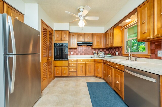 108 56th St, Des Moines, IA 50312 - kitchen with appliances with stainless steel finishes, under cabinet range hood, backsplash, brown cabinetry, and a textured ceiling