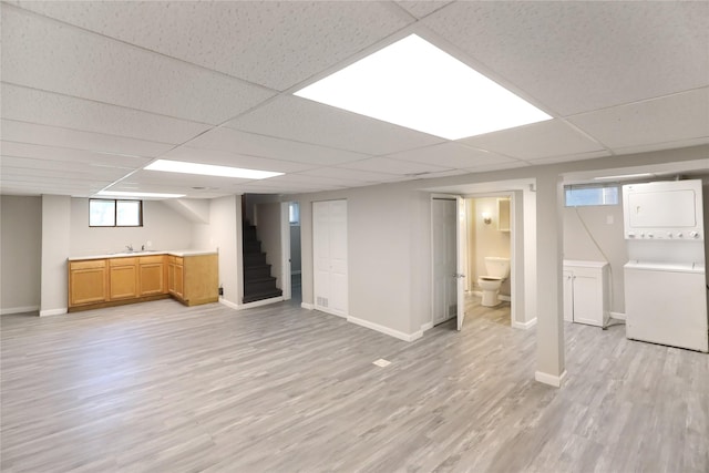 3904 3rd St, Des Moines, IA 50313 - basement with stacked washer / dryer, light wood-style flooring, a drop ceiling, and stairway