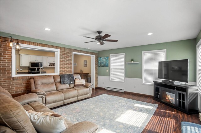 1034 66th St, Windsor Heights, IA 50324 - living area featuring baseboard heating, a wainscoted wall, a ceiling fan, dark wood-type flooring, and healthy amount of natural light