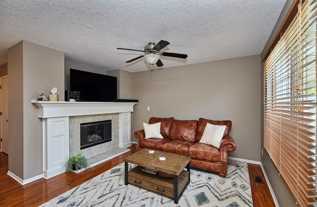 57 SE Meadowlark Ct, Waukee, IA 50263 - living area featuring wood finished floors, a ceiling fan, a tiled fireplace, and a textured ceiling