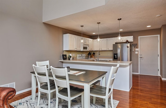 57 SE Meadowlark Ct, Waukee, IA 50263 - kitchen with white appliances, a peninsula, backsplash, dark wood-type flooring, and white cabinets