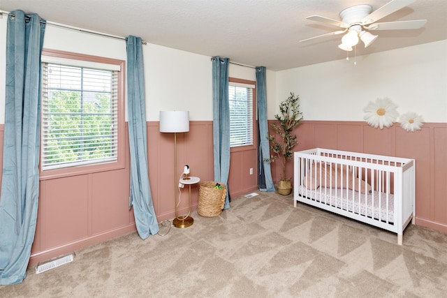12602 Winston Ave, Urbandale, IA 50323 - bedroom with a decorative wall, carpet flooring, wainscoting, a nursery area, and ceiling fan