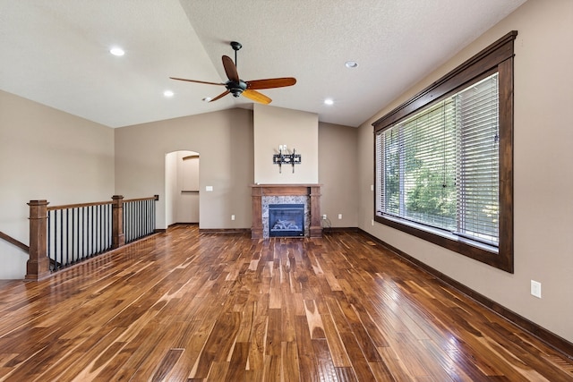 300 NW Sunset Ln, Grimes, IA 50111 - unfurnished living room with ceiling fan, arched walkways, lofted ceiling, wood-type flooring, and a tiled fireplace