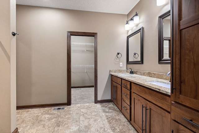 300 NW Sunset Ln, Grimes, IA 50111 - bathroom featuring double vanity, a textured ceiling, and a walk in closet