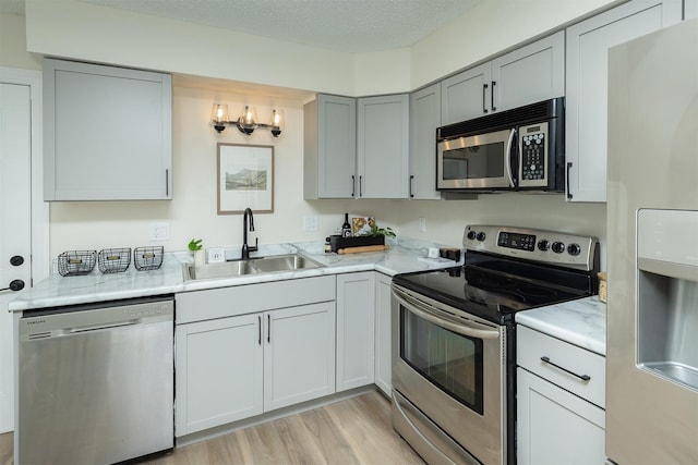 401 NE Harvey St, Grimes, IA 50111 - kitchen featuring stainless steel appliances, gray cabinetry, light wood finished floors, a textured ceiling, and light stone countertops