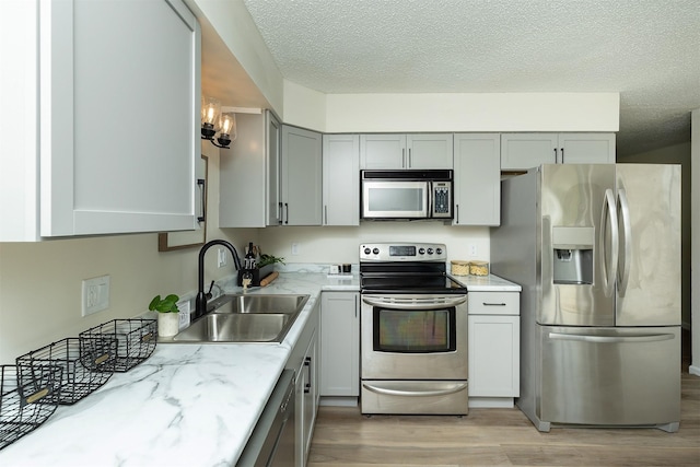 401 NE Harvey St, Grimes, IA 50111 - kitchen featuring appliances with stainless steel finishes, light wood finished floors, a textured ceiling, gray cabinetry, and light stone counters