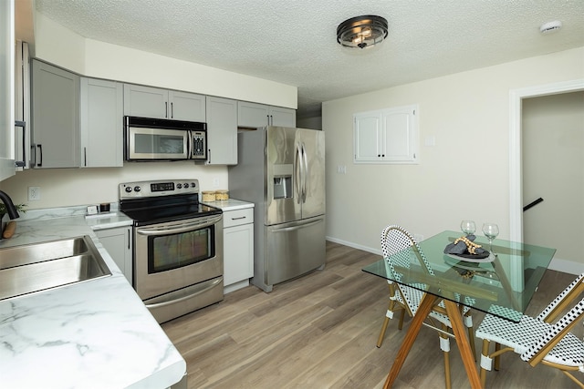 401 NE Harvey St, Grimes, IA 50111 - kitchen with appliances with stainless steel finishes, gray cabinetry, light countertops, light wood finished floors, and a textured ceiling