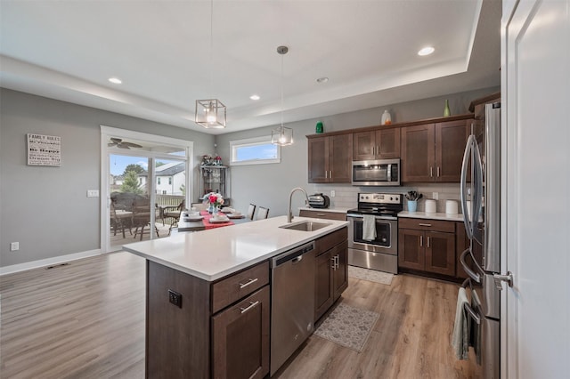 5397 Brook View Ave, Des Moines, IA 50317 - kitchen featuring appliances with stainless steel finishes, a tray ceiling, light wood finished floors, an island with sink, and recessed lighting