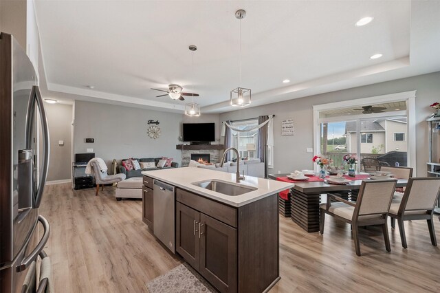 5397 Brook View Ave, Des Moines, IA 50317 - kitchen featuring appliances with stainless steel finishes, a tray ceiling, ceiling fan, dark brown cabinetry, and a stone fireplace