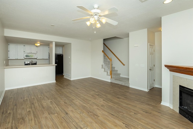 2240 Hart Ave Unit 4, Des Moines, IA 50320 - unfurnished living room with stairs, a ceiling fan, wood finished floors, a tiled fireplace, and recessed lighting