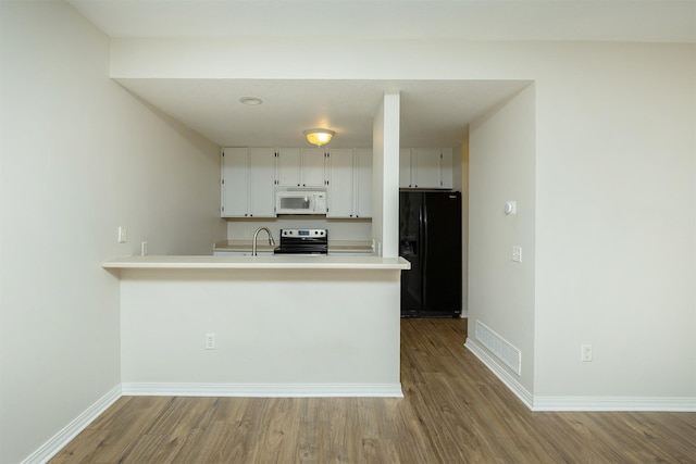 2240 Hart Ave Unit 4, Des Moines, IA 50320 - kitchen with white microwave, black fridge with ice dispenser, range with electric cooktop, wood finished floors, and a peninsula
