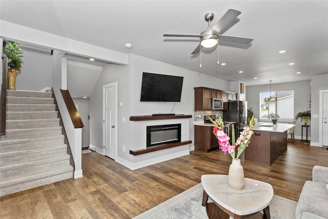 4669 171st St, Urbandale, IA 50323 - living area featuring stairway, dark wood-style floors, recessed lighting, a ceiling fan, and a glass covered fireplace