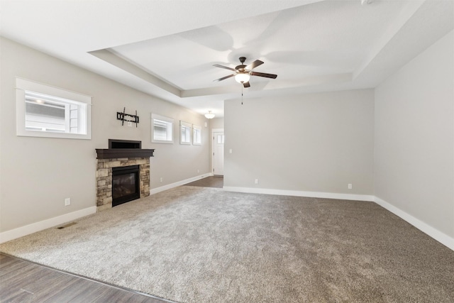 14335 Holcomb Ave, Urbandale, IA 50323 - unfurnished living room featuring a tray ceiling, a stone fireplace, a ceiling fan, carpet, and wood finished floors