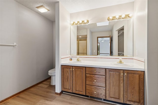 8001 Sheridan Dr, Urbandale, IA 50322 - full bathroom featuring a textured ceiling, double vanity, wood finished floors, a shower with shower door, and a skylight