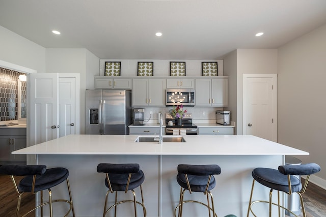1504 NE Savana Dr, Grimes, IA 50111 - kitchen featuring stainless steel appliances, dark wood-style flooring, backsplash, a center island with sink, and a breakfast bar area