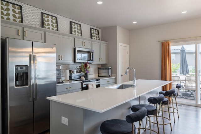 1504 NE Savana Dr, Grimes, IA 50111 - kitchen featuring appliances with stainless steel finishes, an island with sink, a breakfast bar, decorative backsplash, and gray cabinets