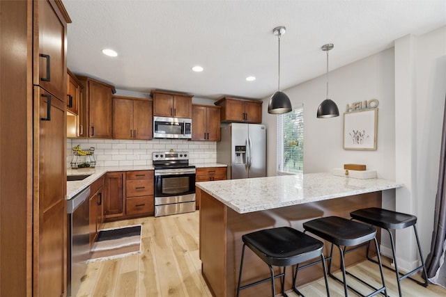 8113 Hammontree Cir, Urbandale, IA 50322 - kitchen with stainless steel appliances, a peninsula, light wood finished floors, brown cabinetry, and recessed lighting